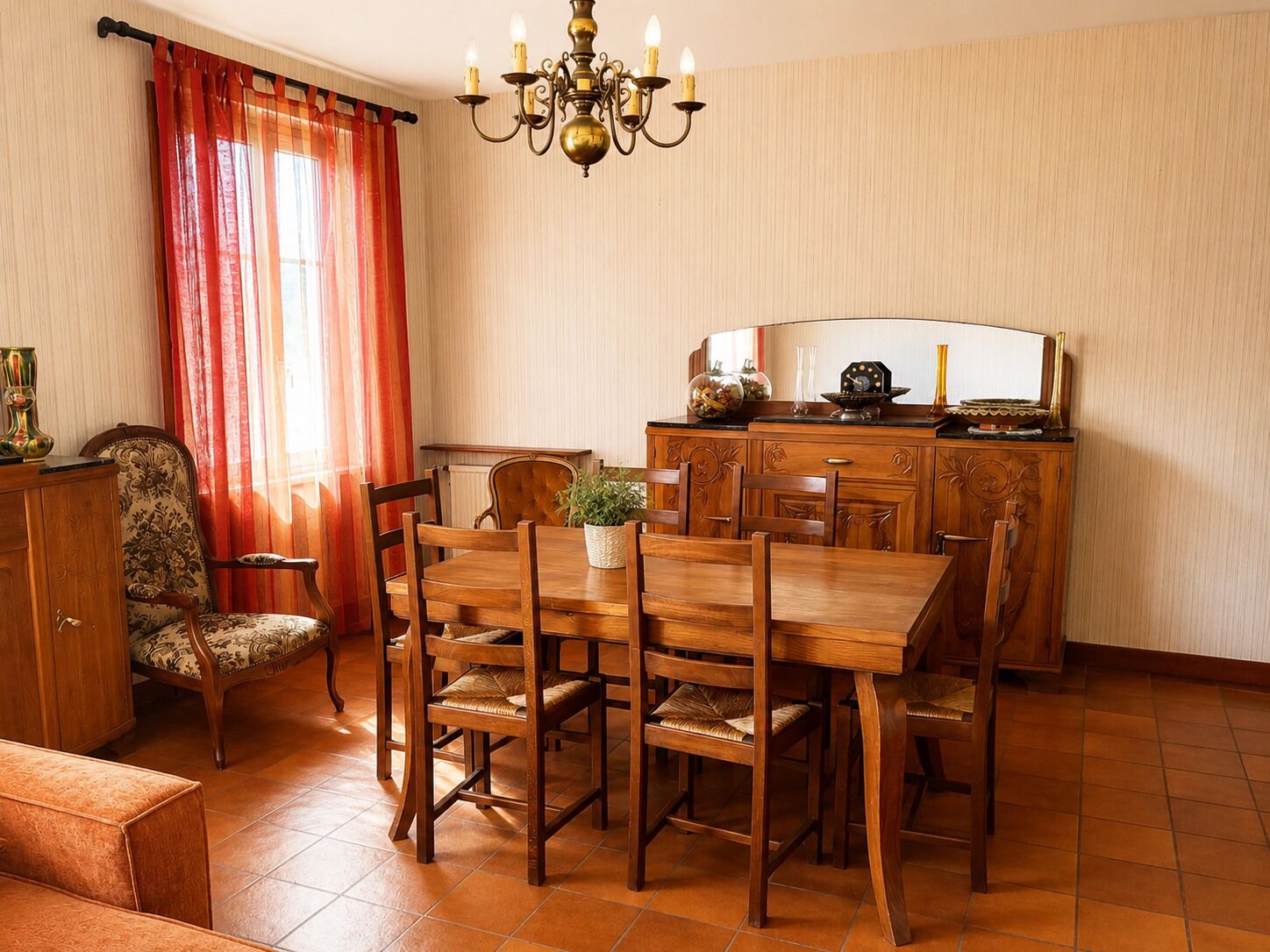 Uma sala de jantar com mesa e cadeiras de madeira, um lustre, uma cortina vermelha e um armário com objetos decorativos.