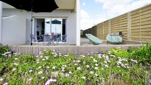 A patio with a table and chairs, a black umbrella, and a wooden fence. - Swimming pool with a 100-meter cable winch, located 100 meters from the beach* (Guidel)