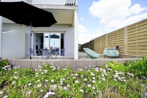A patio with a table and chairs, a black umbrella, and a wooden fence. - Swimming pool with a 100-meter cable winch, located 100 meters from the beach* (Guidel)