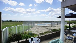 An outdoor patio area with a pool, surrounded by a metal fence, and a view of the landscape. - Swimming pool with a 100-meter cable winch, located 100 meters from the beach* (Guidel)