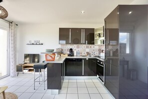 A modern kitchen with a central island, built-in appliances, and a large window. - Swimming pool with a 100-meter cable winch, located 100 meters from the beach* (Guidel)