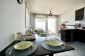 A dining area with a table set for two, a kitchen with a flat-screen TV, and a balcony with a view. - Swimming pool with a 100-meter cable winch, located 100 meters from the beach* (Guidel)