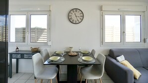 A dining area with a table set for four, a clock on the wall, and a sofa in the background. - Swimming pool with a 100-meter cable winch, located 100 meters from the beach* (Guidel)