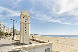Ein Glockenturm an einer Promenade mit Blick auf einen Strand, im Hintergrund sind Gebäude zu sehen.