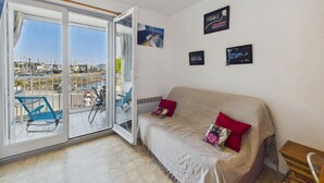 Et værelse med en skydedør ud til en balkon, en sofa med puder og billeder hængende på væggen.