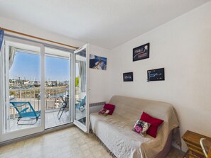 Ein Zimmer mit einer Glasschiebetür, die auf einen Balkon führt, einer Couch mit Kissen und gerahmten Bildern an der Wand.