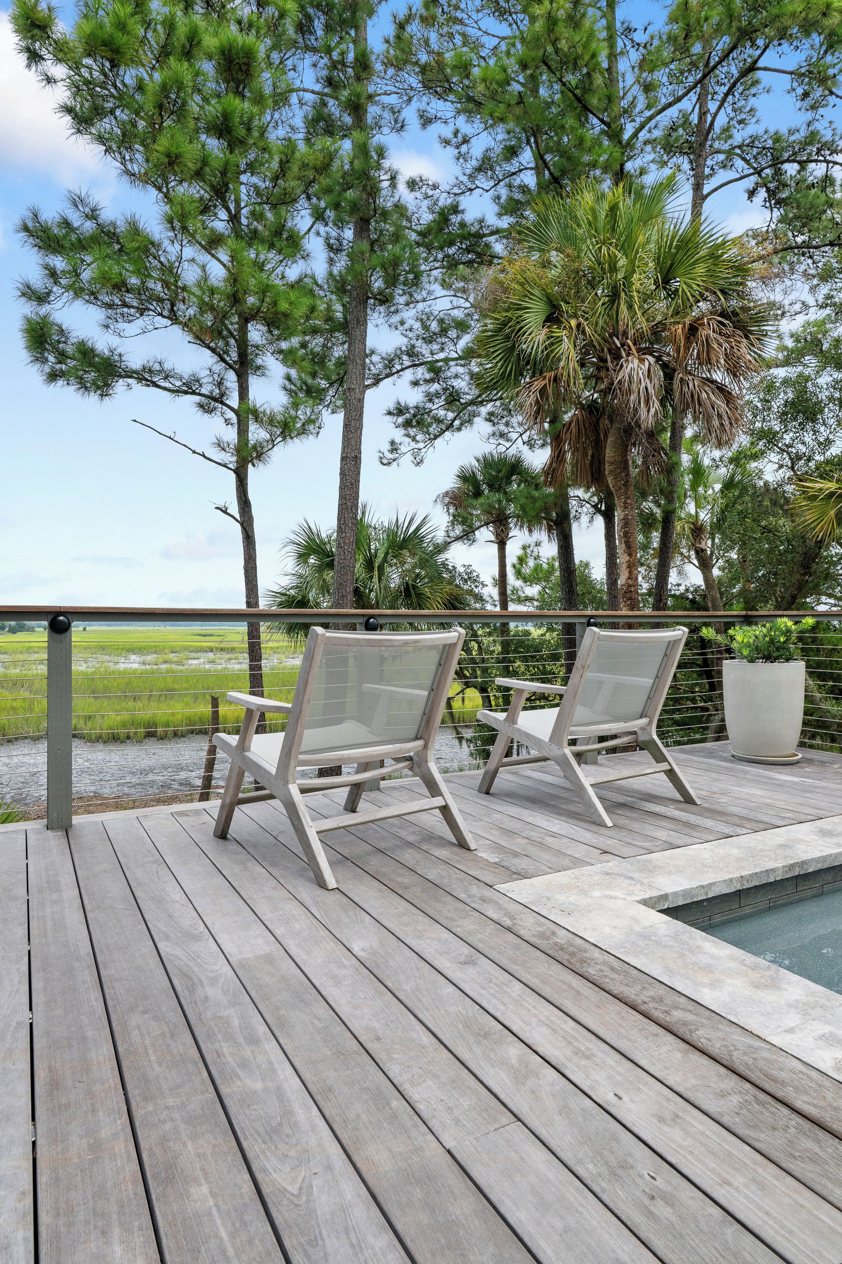 A wooden deck with two white chairs and a small pool.