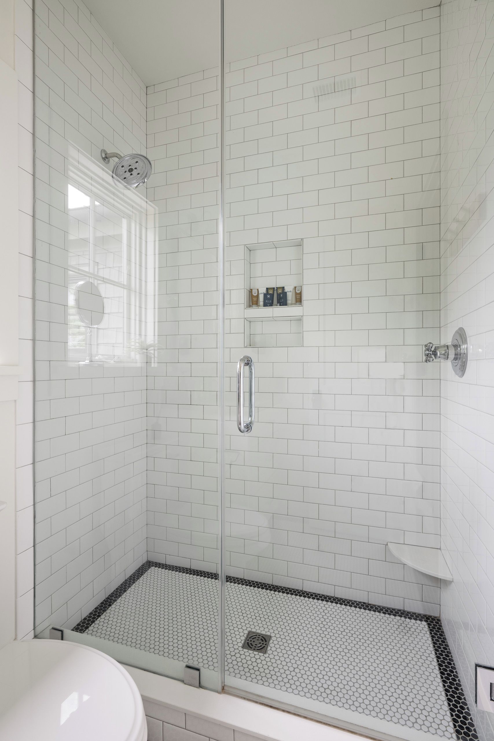 A glass-enclosed shower with white subway tiles, a glass door, and a black and white hexagonal floor pattern.