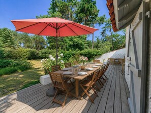 Eine Terrasse aus Holz mit einem Esstisch, gedeckt für vier Personen, umgeben von Stühlen und einem roten Sonnenschirm.