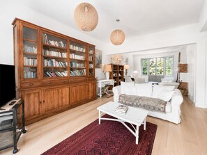 Ein großzügiges Wohnzimmer mit einem großen Bücherregal aus Holz, einem weißen Sofa, einem Couchtisch und einem roten Teppich mit Muster.