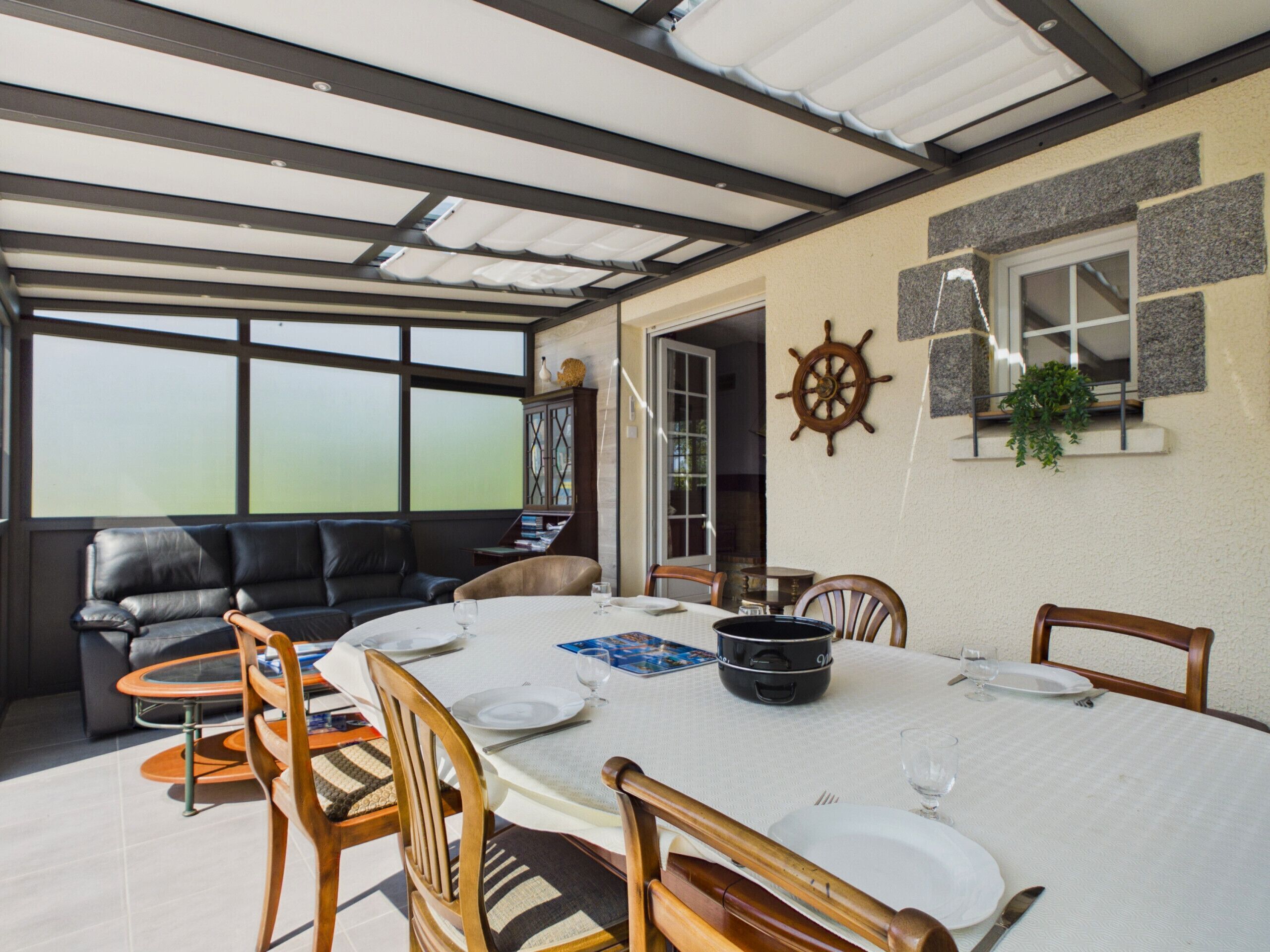 A dining area with a table set for four, surrounded by wooden chairs, a black leather sofa, and a bookshelf.
