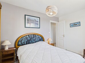 A bedroom with a bed, a nightstand, a lamp, a door, and two framed pictures on the wall. - House for 8 p, 400m from the beach, Kerlouan (Kerlouan)