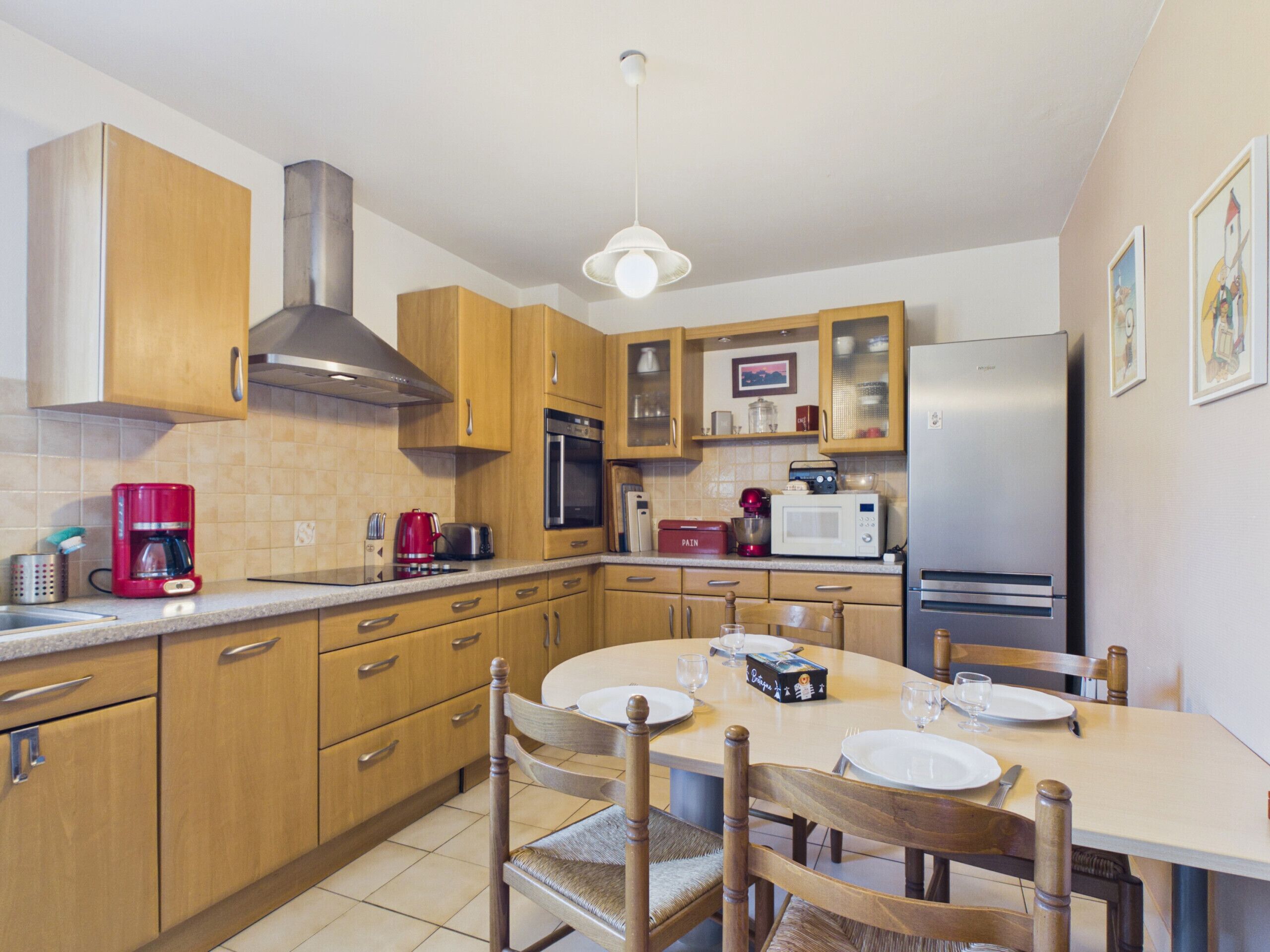 Een moderne keuken met houten kastjes, een roestvrijstalen koelkast en een eettafel voor vier personen.