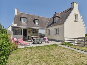 Ein zweistöckiges Haus mit einer Terrassenfläche, auf der Gartenmöbel stehen.