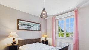 Et soveværelse med en træseng, to sengeborde med lamper, et vindue med pink gardiner og et billede på væggen.