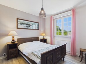 Ein Schlafzimmer mit einem hölzernen Bett, zwei Nachttischen mit Lampen, einem Fenster mit rosa Vorhängen und einem Bild an der Wand.