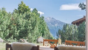 A room with a view of a mountain and trees. There are wooden chairs and a table with a white tablecloth. - Cozy, Alpine • Terrace • Indoor parking (Val de Bagnes)
