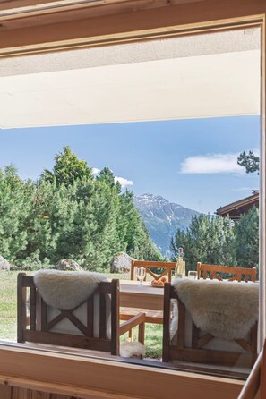 A room with a view of a mountain and trees. There are wooden chairs and a table with a white tablecloth. - Cozy, Alpine • Terrace • Indoor parking (Val de Bagnes)