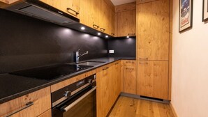 A modern kitchen with wooden cabinets, a black countertop, stainless steel sink, and built-in oven. - Cozy, Alpine • Terrace • Indoor parking (Val de Bagnes)