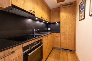 A modern kitchen with wooden cabinets, a black countertop, stainless steel sink, and built-in oven. - Cozy, Alpine • Terrace • Indoor parking (Val de Bagnes)