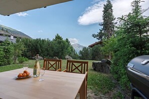 An outdoor dining table with chairs, a bottle of wine, and a glass, set against a backdrop of trees and mountains. - Cozy, Alpine • Terrace • Indoor parking (Val de Bagnes)