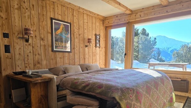 A wooden-paneled room with a bed, a side table, and a large window offering a mountain view. - Cozy, Alpine • Terrace • Indoor parking (Val de Bagnes)