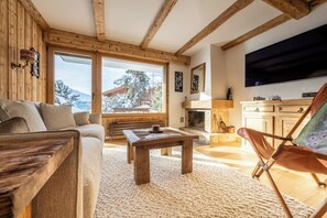 A cozy living room with a sofa, a wooden coffee table, a fireplace, and a large window offering a mountain view. - Cozy, Alpine • Terrace • Indoor parking (Val de Bagnes)