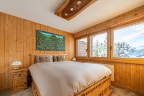 Een houten kamer met een bed, een nachtkastje, een raam met uitzicht op bomen en een schilderij aan de muur.
