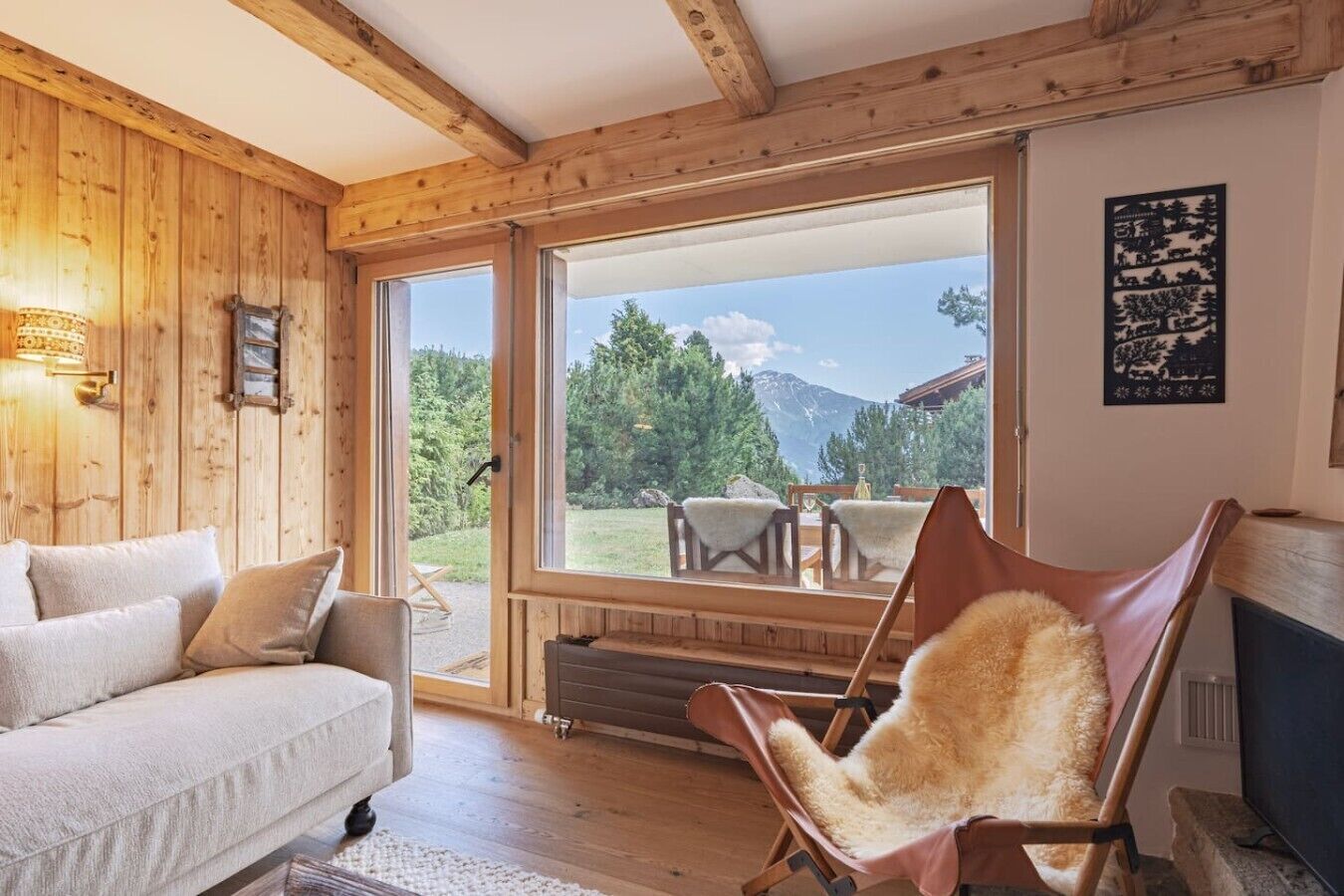 Une pièce chaleureuse au décor intérieur en bois, avec un canapé, un fauteuil recouvert de fourrure et une grande fenêtre donnant sur l’extérieur.