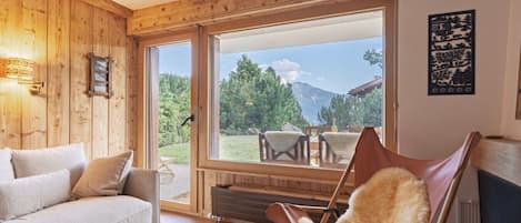 Una habitación acogedora con detalles de madera, un sofá, un sillón cubierto de piel y un ventanal con vistas al exterior.