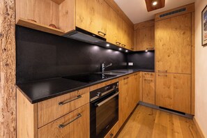 Eine moderne Küche mit Holzschränken, einer schwarzen Arbeitsplatte, Edelstahlgeräten und einem eingebauten Backofen.