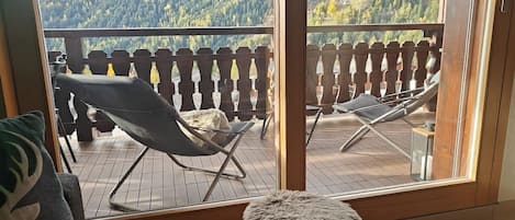 A balcony with a wooden railing, two lounge chairs, and a small stool.
