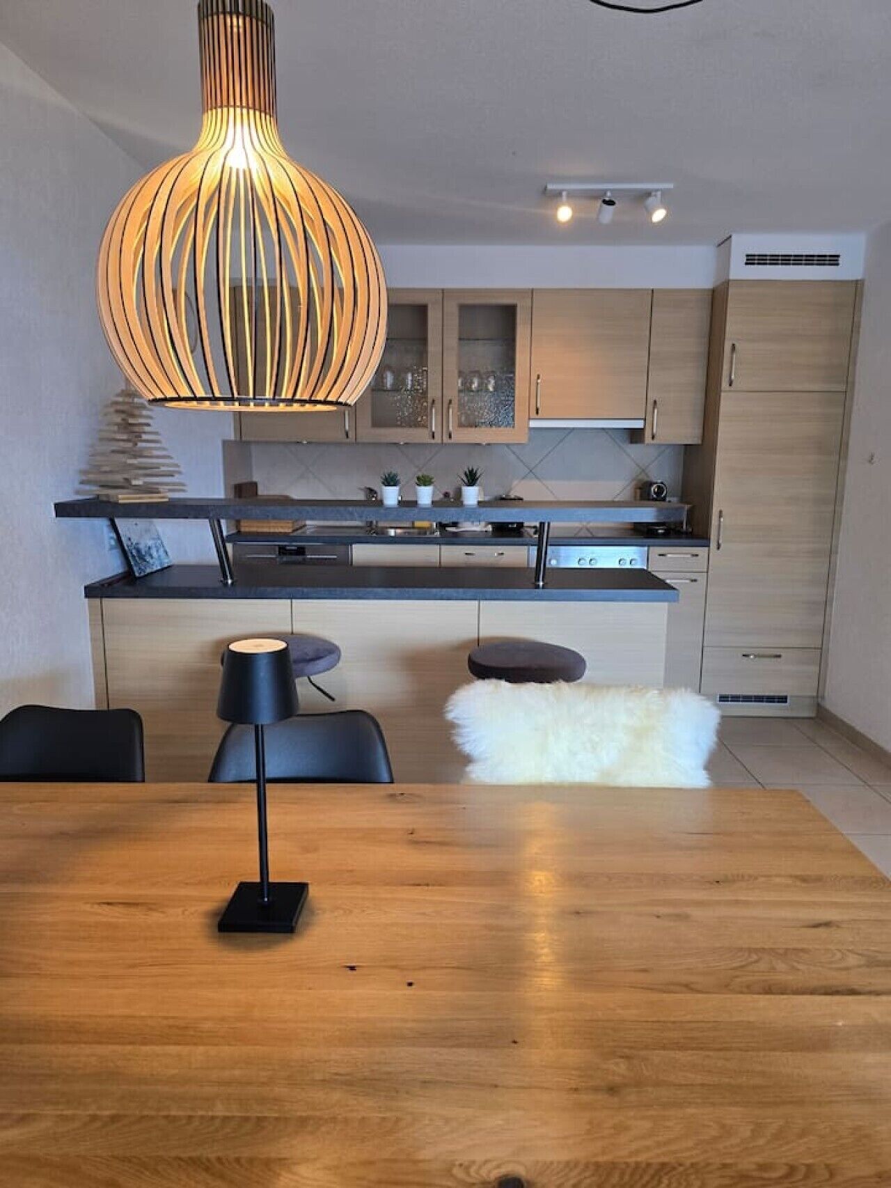 Eine moderne Küche mit Kochinsel, Pendelleuchten und einem Essbereich mit Holztisch und -stühlen.