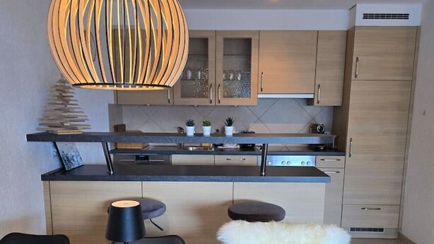 Een moderne keuken met een centraal eiland, hangende verlichting en een eethoek met een houten tafel en stoelen.