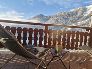 Eine Holzterrasse mit Blick auf schneebedeckte Berge. Zwei Liegestühle und ein Tisch mit einer Kerze sind aufgestellt.