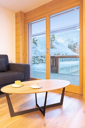 Una habitación con una mesa de madera, un sofá y un ventanal corredero que da a un espacio exterior nevado.
