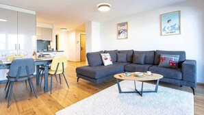 A modern living room with a grey sofa, a round coffee table, and a dining area with a yellow chair. - Ski-in/Ski-out • Mountain View • Spa & Sauna (Nendaz)