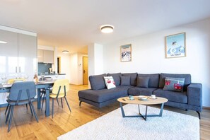 Ein modernes Wohnzimmer mit einem grauen Sofa, einem runden Couchtisch und einem Essbereich mit einem gelben Stuhl.