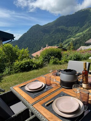 An outdoor dining table set with plates, cutlery, and glasses, overlooking a mountainous landscape. - Cozy & Bright • 1 Bedroom • Ovronnaz (Leytron)