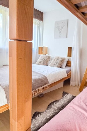 A bedroom with a bed, a wooden headboard, a bedside table, a wall-mounted artwork, and a window with curtains. - Cozy & Bright • 1 Bedroom • Ovronnaz (Leytron)