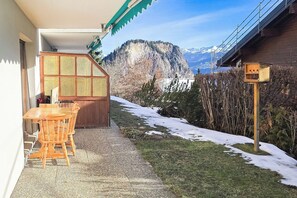 Zona d'estar exterior de fusta amb taula i cadires, un porxo cobert i vistes a una serralada.