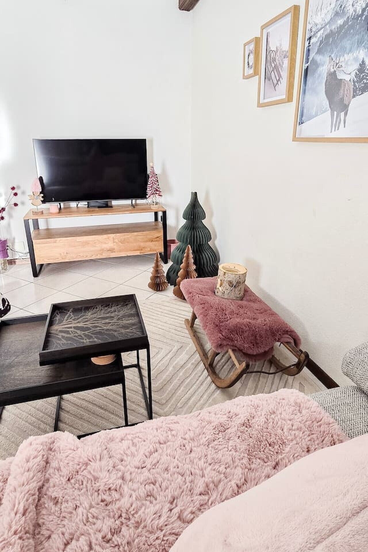 Un salon chaleureux avec un téléviseur à écran plat, une table basse en bois, un canapé rose moelleux, un petit fauteuil à bascule en bois et un sapin de Noël.
