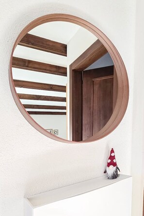 A round mirror with a wooden frame on a white wall. - Cozy & Bright • 1 Bedroom • Ovronnaz (Leytron)