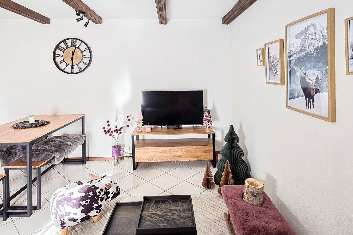 Un salon moderne avec une table basse en bois, un téléviseur posé sur un meuble en bois, une horloge au mur et des tableaux encadrés.