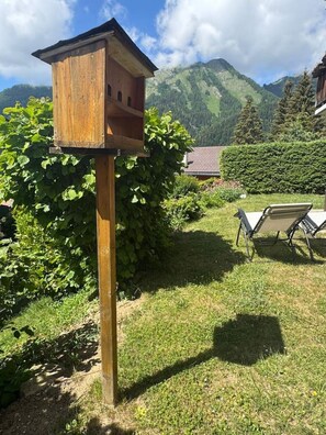 A wooden birdhouse on a post in a garden with a mountain backdrop. - Cozy & Bright • 1 Bedroom • Ovronnaz (Leytron)