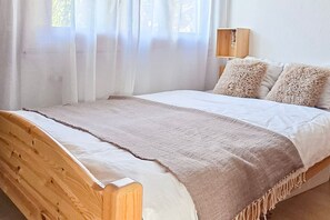 A bed with a wooden headboard, a beige blanket, and two fluffy pillows. - Cozy & Bright • 1 Bedroom • Ovronnaz (Leytron)