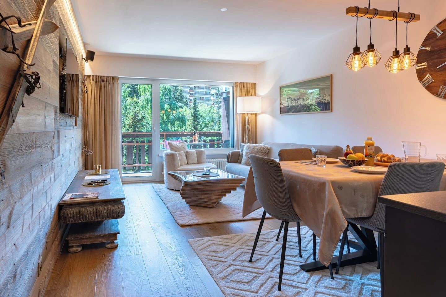 Un espace de repas moderne avec une table dressée pour deux personnes, un canapé et une grande fenêtre donnant sur un paysage verdoyant.