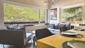 Een modern interieur met een eethoek, een bank en grote ramen met uitzicht op een bebost landschap.