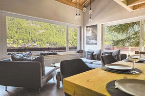 Ein modernes Interieur mit Essbereich, Sofa und großen Fenstern mit Blick auf eine bewaldete Landschaft.