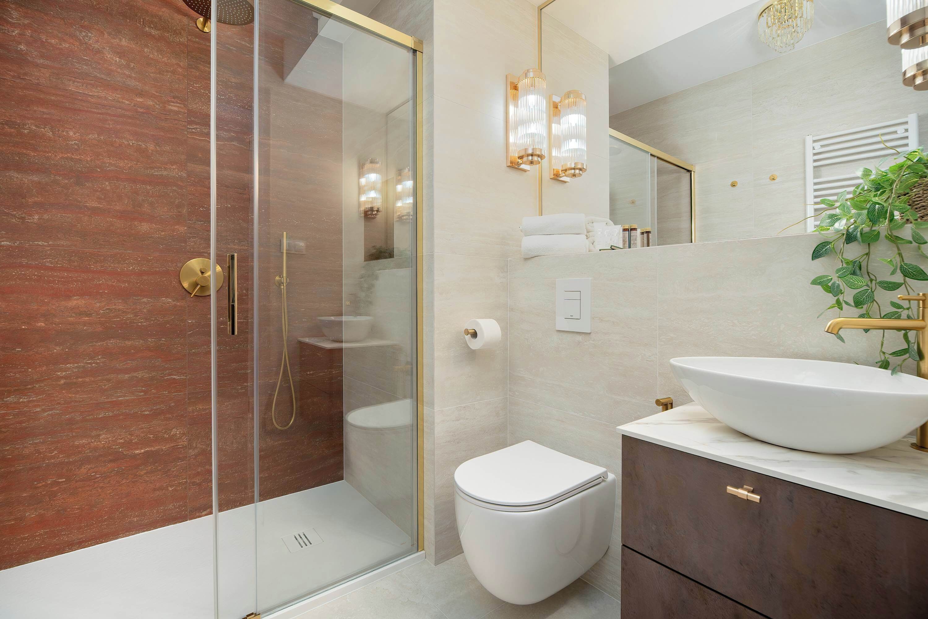 A modern bathroom with a glass-enclosed shower, a white toilet, a large vessel sink, and a mirror with a plant.